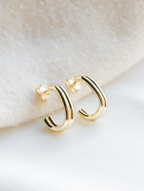 une paire de boucles d'oreilles en or posée sur une couverture blanche