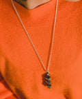 une femme portant un pull orange et un long collier en pierre