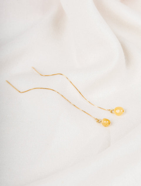 une paire de boucles d'oreilles jaunes posées sur un tissu blanc